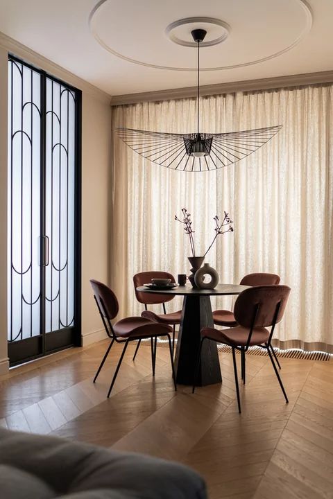 a Parisian chic dining nook by the window with chevron flooring, a black table, burgundy chairs and a black pendant lamp