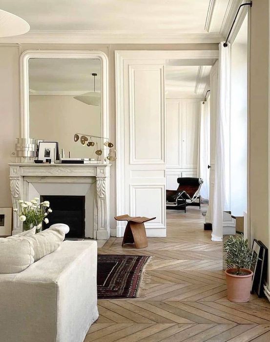 a Parisian living room with a chevron floor, a fireplace, neutral seating furniture, a wooden stool and some decor and plants
