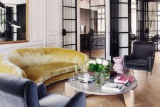 a beautiful Parisian livng room with molding and chevron floors, a mustard sofa, a blue chair, a statement mirror in an ornated frame