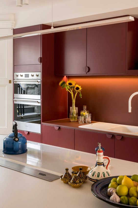 A beautiful and elegant burgundy kitchen with built in lights, a kitchen island with white stone countertops and a pendant lamp