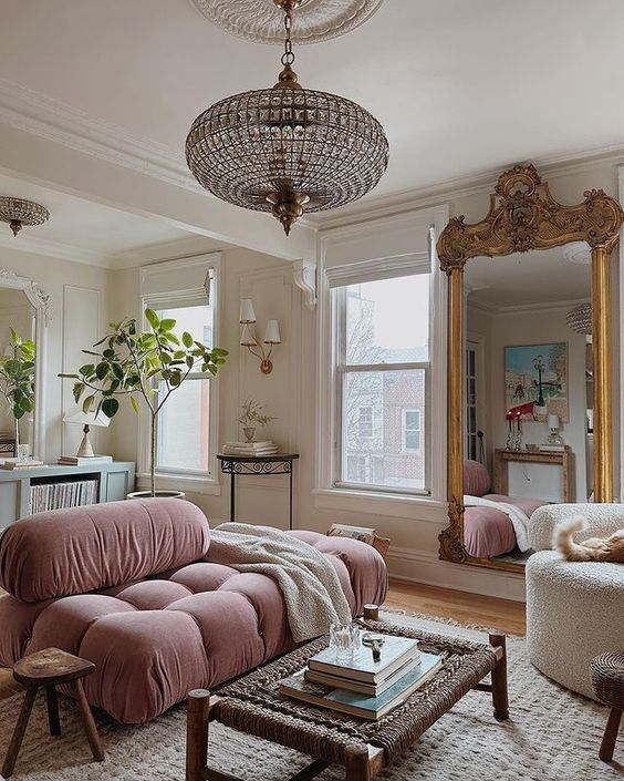 a beautiful and whimsical living room with neutral walls, a dusty pink low sofa, a mirror in an ornated frame, a jute table and a crystal sphere chandelier