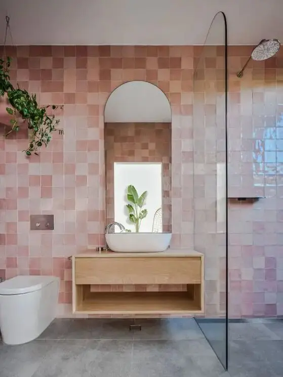 a beautiful bathroom clad with pink zellige tiles, a shower, a floating vanity, an arched mirror and some greenery