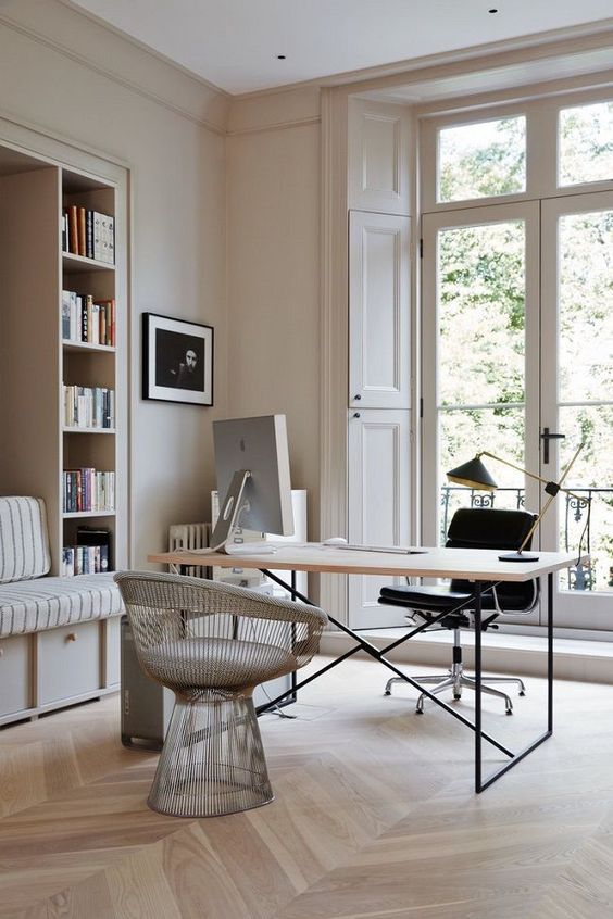 A beautiful neutral home office with built in shelves and a seat, a desk, a black chair and a neutral one, some decor and books