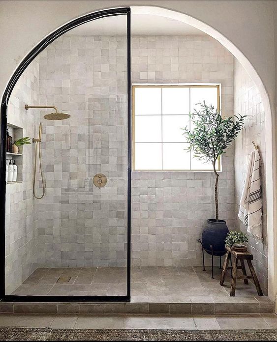 a beautiful shower space clad with Zellige tiles, with a window, an arched door and some potted plants