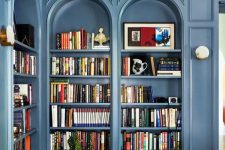 a beautiful space with blue arched bookcases and molding, a navy stool and a yellow seat for reading here