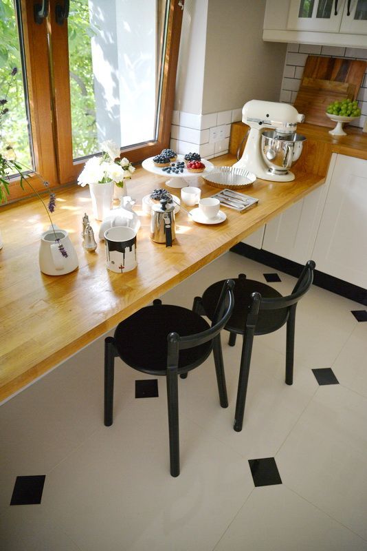 a beautiful white kitchen with a stained windowsill as a table and black chairs and matching stained countertops is pretty and cool