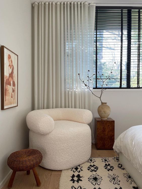 a bedroom with a single white boucle chair, a side table with a lovely vase and branches and a rattan side table