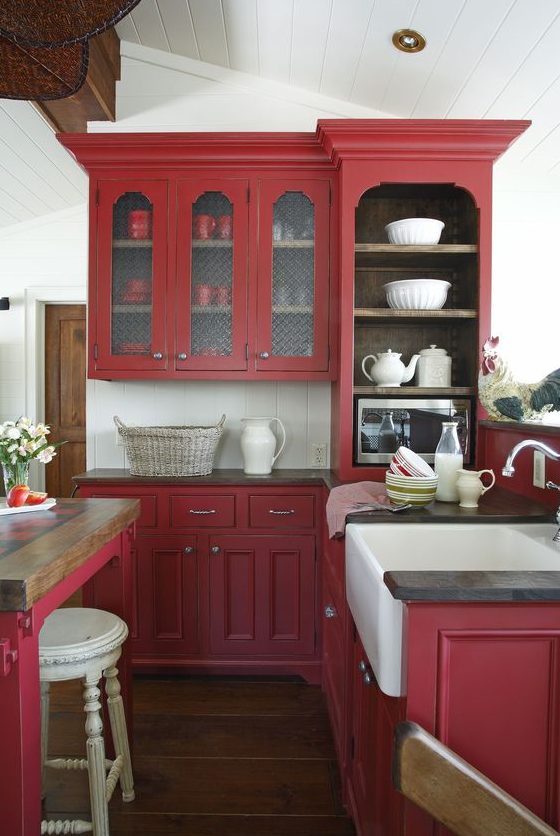 a berry red vintage kitchen with white tiles, black countertops and a vintage table as a table and kitchen island