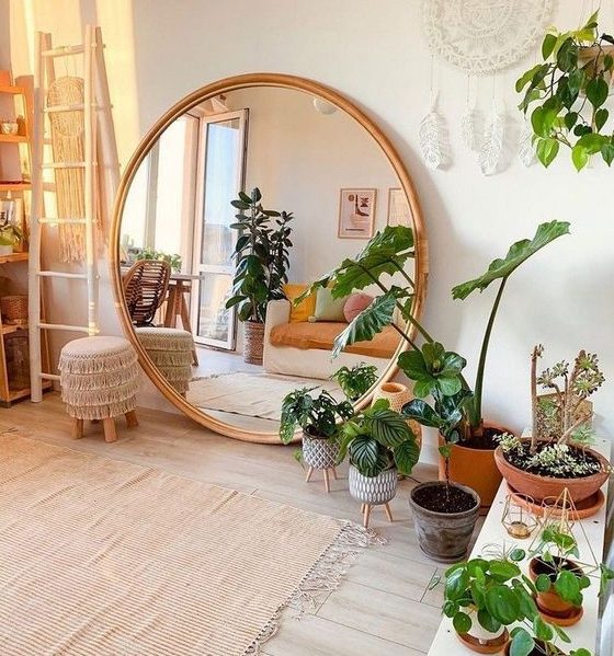 a boho chic living room in neutrals, with lots of potted greenery and an oversized round mirror