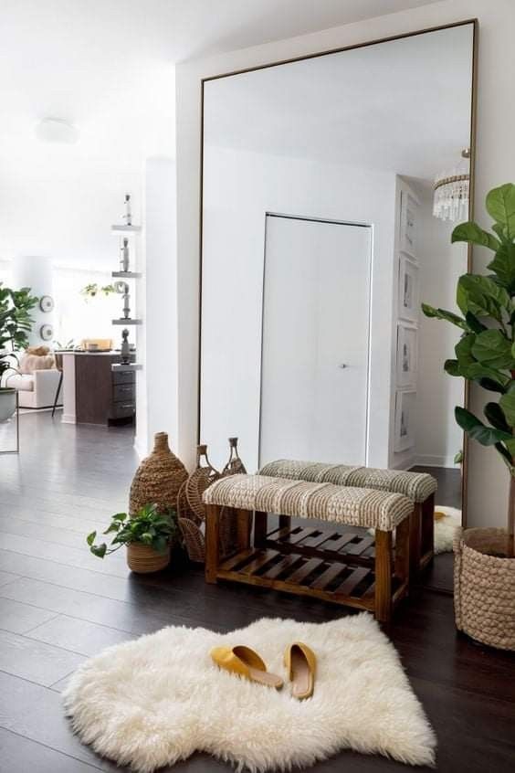 a boho nook with an oversized mirror that takes a whole wall, a woven bench, a rug, potted plants