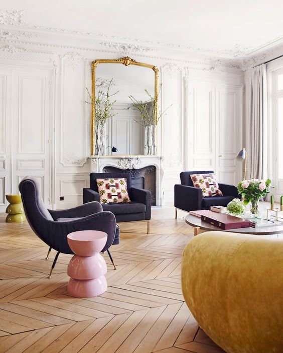 a bold French chic living room with molding, parquet flooring, navy chairs, a mustard sofa anda pink and yellow side table