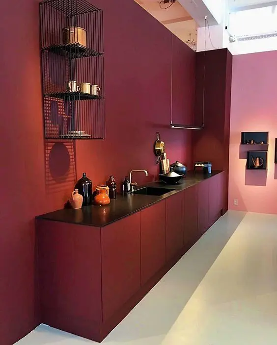 a bold and minimal burgundy kitchen with burgundy walls and cabinets, black countertops, metal shelves and pendant lamps