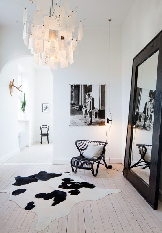 a bold black and white Nordic space with a black rattan chair, an oversized mirror in a black frame, a catchy note chandelier
