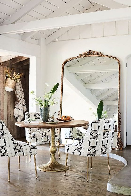 a bold dining space with a round table and printed chairs, an oversized mirror in a gilded frame and potted plants
