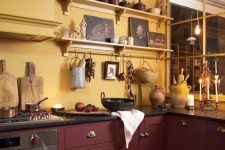 a bold kitchen with mllow yellow walls, burgundy cabinets, black countertops and lots of beautiful vintage decor