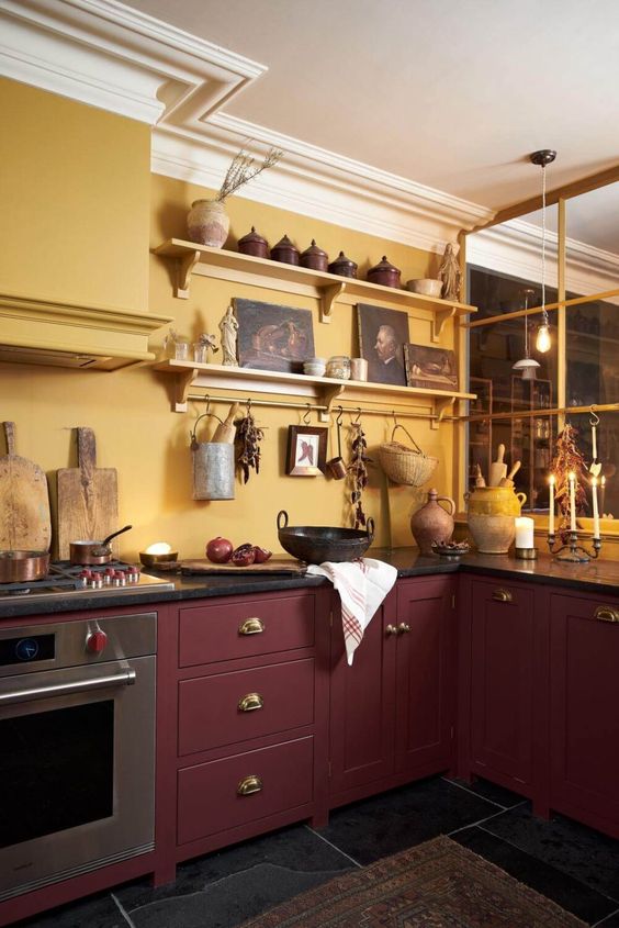 a bold kitchen with mllow yellow walls, burgundy cabinets, black countertops and lots of beautiful vintage decor
