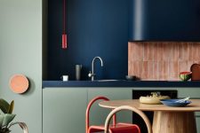 a bold kitchen with olive green cabinetry, a navy and pink stacked tile backsplash, a navy hood, a stained table and a pink tile floor