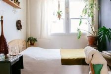 a bright boho bedroom with a stained bed, a bold rug, a desk, a chair, a table, potted plants and some wood