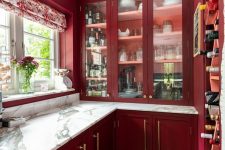 a bright burgundy kitchen with shaker cabinets and white marble countertops, a printed curtain is a chic and bold space