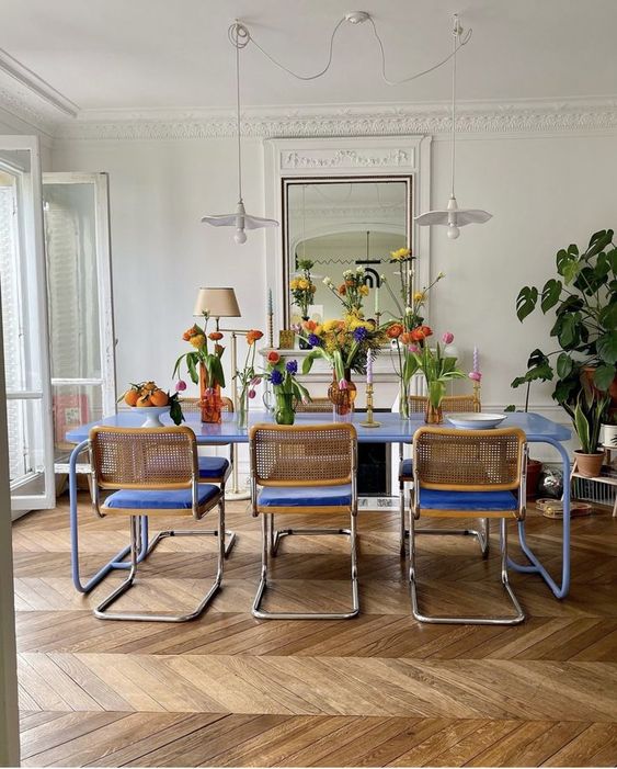 a bright dining room with molding and chevron flooring, a bold blue table and chairs, pendant lamps and colorful blooms