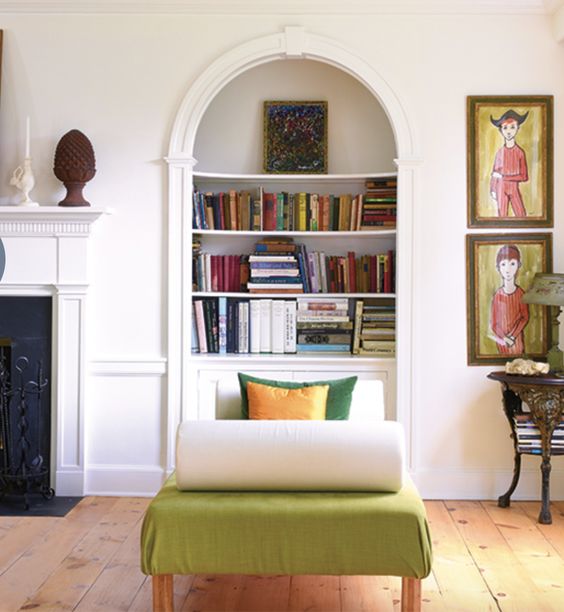 A built in arched bookcase, a green daybed with pillows, artwork and a side table with a lamp as a reading nook