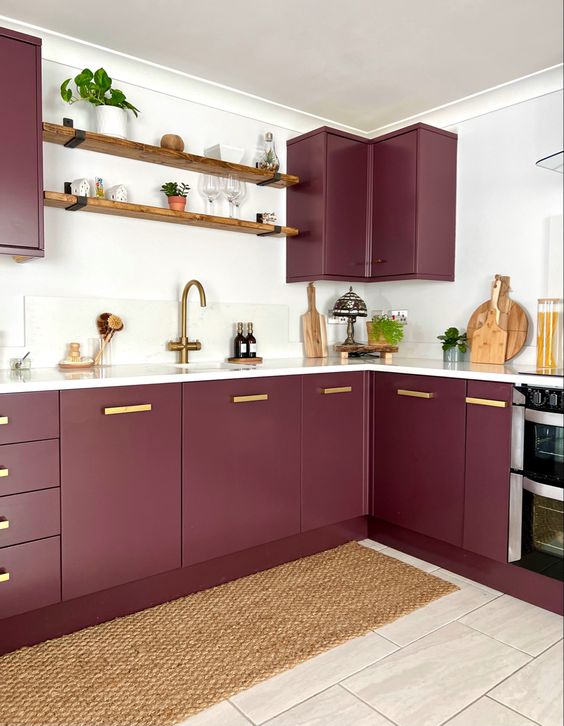 a burgundy plum kitchen with white countertops and a backsplash, open shelves and gold handles