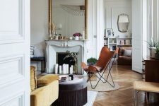 a chic Parisian living room with chevron flooring, a fireplace with candles, a yellow sofa, an amber chair, an ottoman and a mirror