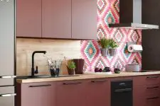 a chic burgundy kitchen with matte panels, a wood and bold tile backsplash, black handles and a dark hood