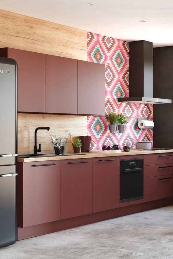 a chic burgundy kitchen with matte panels, a wood and bold tile backsplash, black handles and a dark hood
