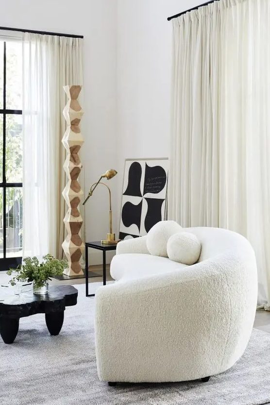 a chic contemporary living room with a creamy boucle sofa, a black table and some art, neutral drapes
