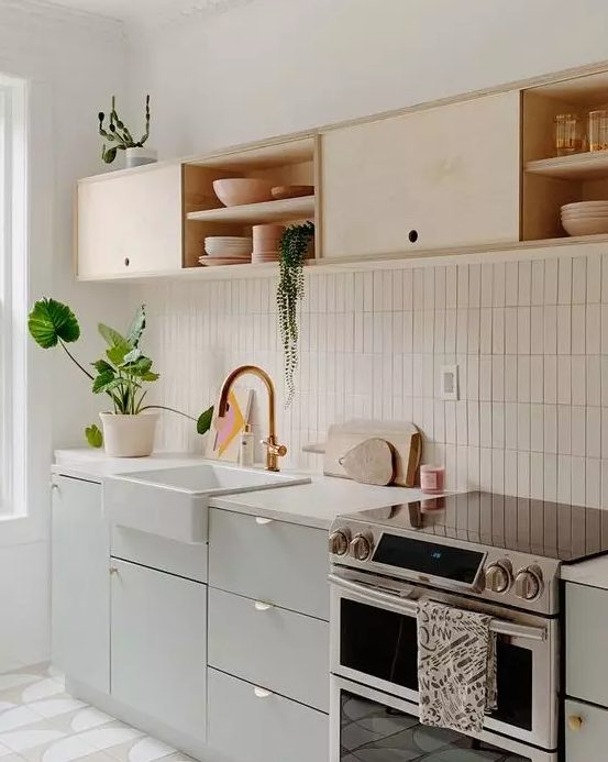 A chic kitchen in dove grey and light colored plywood, with white countertops and a white stacked tile backsplash