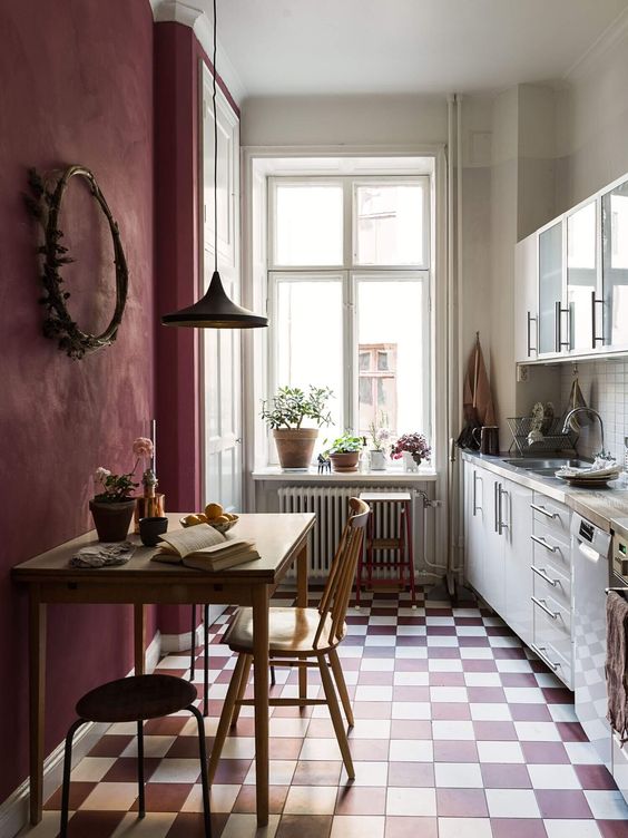 a chic kitchen with a burgundy textural wall, stained dining furniture, white cabinets and butcherblock countertops