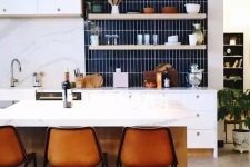 a chic modern white kitchen with a navy skinny tile backsplash and amber leather stools