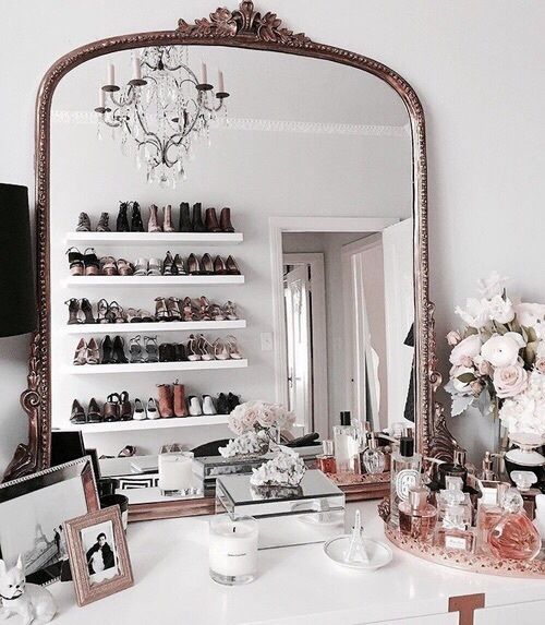 a closet with an oversized mirror in an ornated frame, some storage units and open shoe shelves