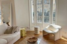 a contemporary Parisian chic living room with white seating furniture, a glass coffee table and a side table