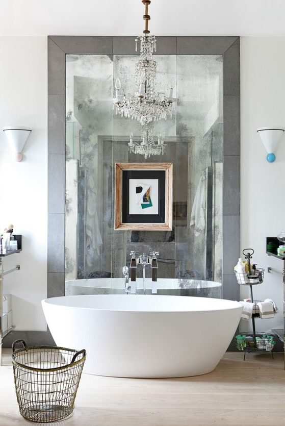 a contemporary bathroom in neutral shades, an oval tub, a large mirror in tiles, a crystal chandelier