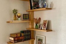 a corner shelving unit with books, photos, decor and dried grasses is a cool solution for a modern space