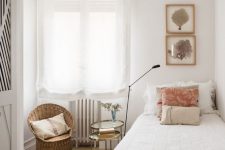 a cute narrow guest bedroom with a bed and neutral bedding, a rattan chair, a tiered side table and some decor on the wall