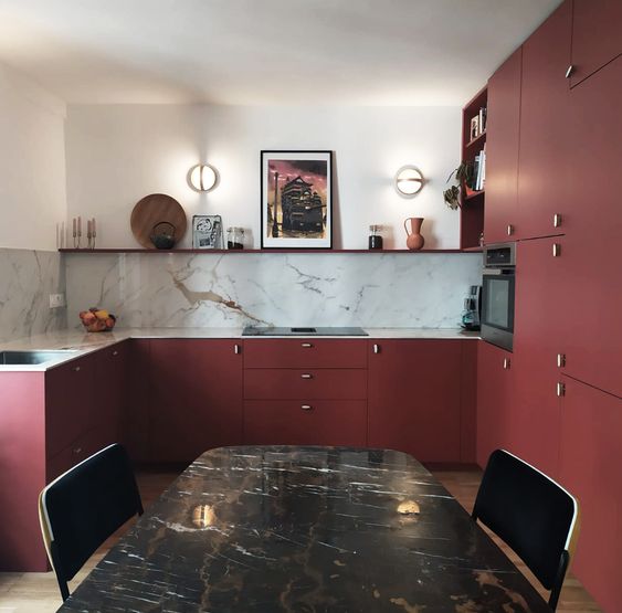 a deep burgundy matte kitchen with an elegant marble backsplash and an open shelf, a table and black chairs