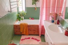 a dopamine decor bathroom clad with green and white tiles, a tub done with wood, a blush vanity, a pink curtain and rug