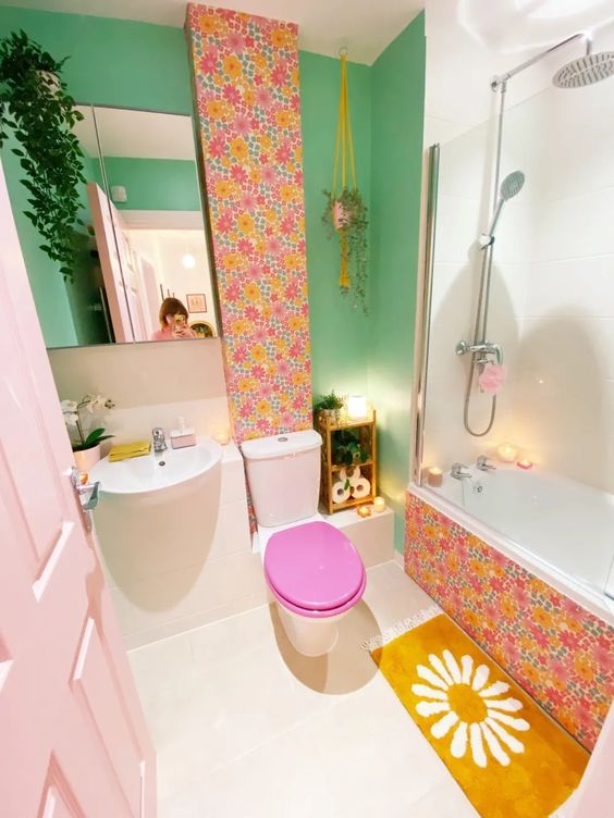 a dopamine decor bathroom with a green wall, wallpaper accents, a mustard rug, greenery and a blush door
