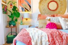 a dopamine decor bedroom with a bed and bold coral and blue bedding, a bedside and corner table, bold artwork and greenery