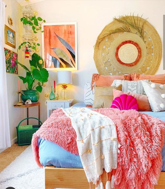 a dopamine decor bedroom with a bed and bold coral and blue bedding, a bedside and corner table, bold artwork and greenery