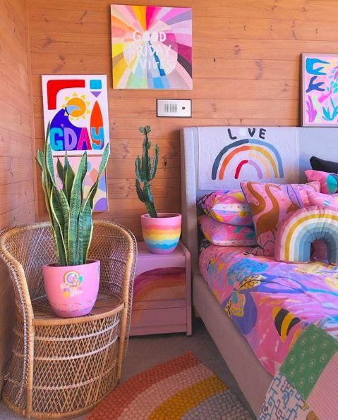 a dopamine decor bedroom with a bed done with extra bold bedding, pink nightstands, potted plants and bright artwork