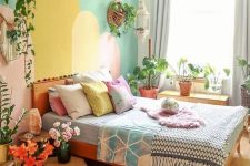 a dopamine decor bedroom with a cool and colorful accent wall, a bed with pastel bedding, blooms, a pendant lamp and greenery