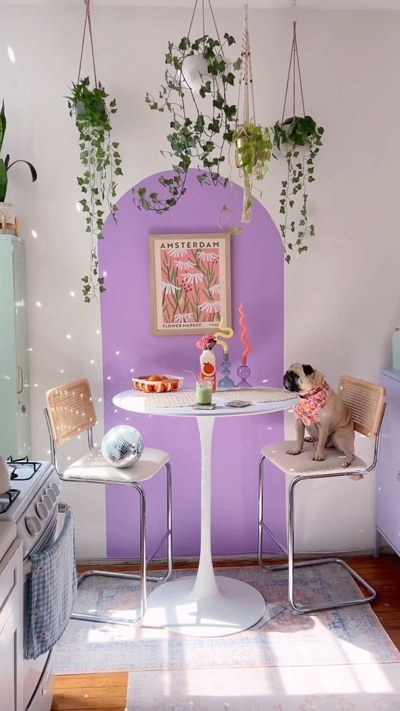 a dopamine decor dining nook with a purple accent, a table and rattan chairs, potted plants and a disco ball on the chair