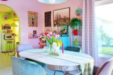 a dopamine decor dining room with blush walls, a table and turquoise and lilac chairs, a bold gallery wall and a green pendant lamp