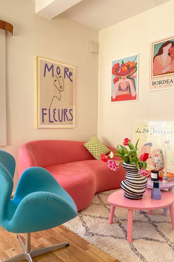 a dopamine decor living room with a coral curved sofa, a blue chair, a pink coffee table, bold artwork and some decor