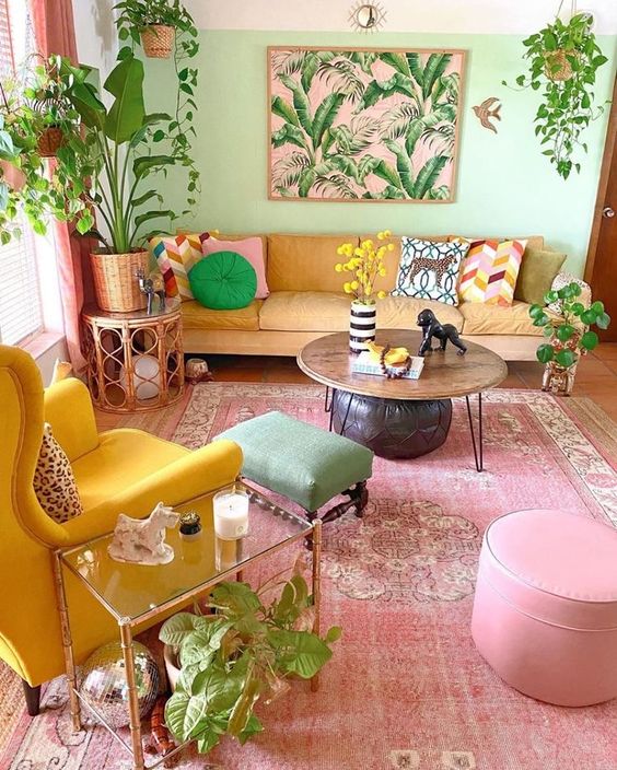 a dopamine decor living room with a light green accent wall, a yellow sofa, a bold yellow chair, a pink rug and pouf plus a green stool