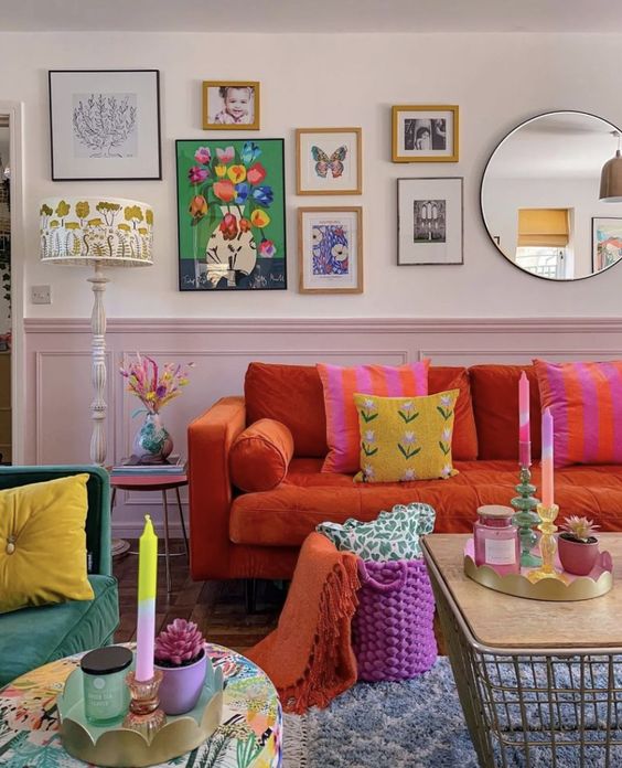 a dopamine decor living room with blush paneling, an orange sofa and colorful pillows, a hot pink basket, a pretty gallery wall